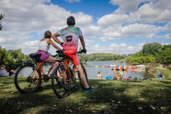 Couple à vélo qui s'arrête regarder le paysage de l'Île de loisirs et promeneurs allongés dans l'herbe