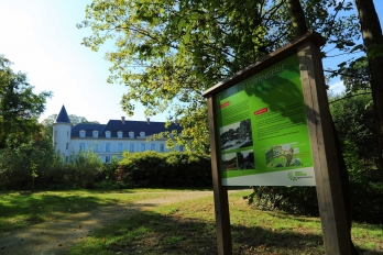 Parc du château de Menucourt, avec le château au fond et un panneau d'information sur le jardin de l'orangerie au premier plan