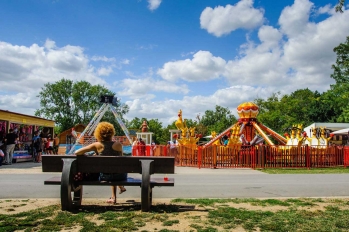 Personne de dos assise sur un banc qui regarde les manèges pour enfants à l'Île de loisirs de Cergy-Pontoise